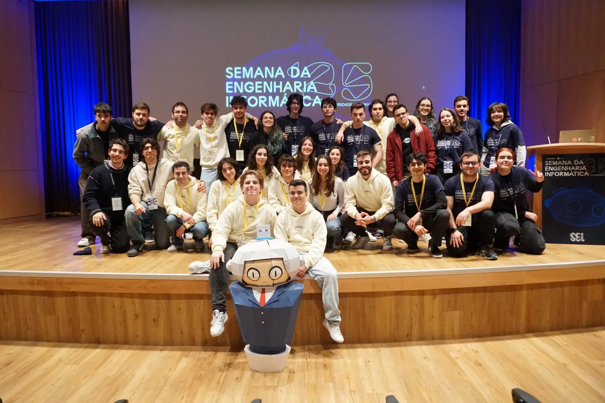 Grupo de estudantes do CeSIUM reunidos no palco durante a Semana da Engenharia Informática, com a mascote Void.